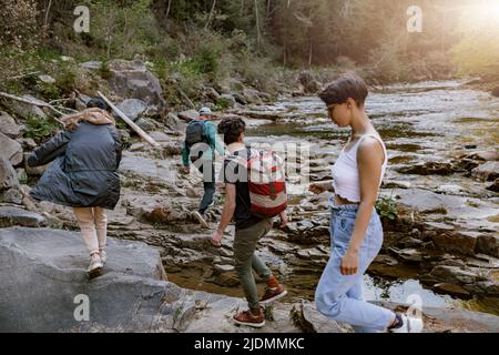 Back view on young men and women hikers trekking the river valley in mountains. Hiking. Stock Photo