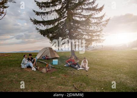 Two happy couples having fun with music at vamp site in mountains. On rural tour. Stock Photo