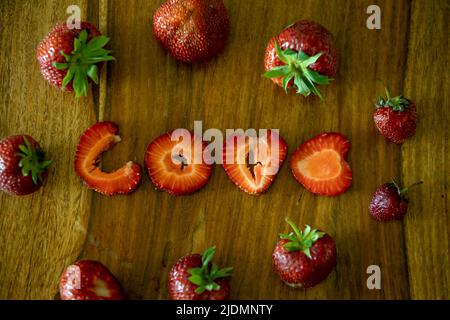 Love sign made from strawberry pieces on a table, whote strawberries around it Stock Photo