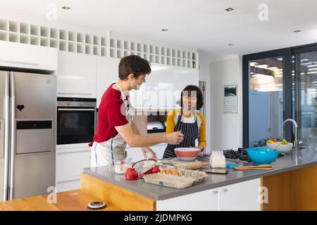 Multiracial happy young couple wearing aprons making bread on kitchen island, copy space Stock Photo
