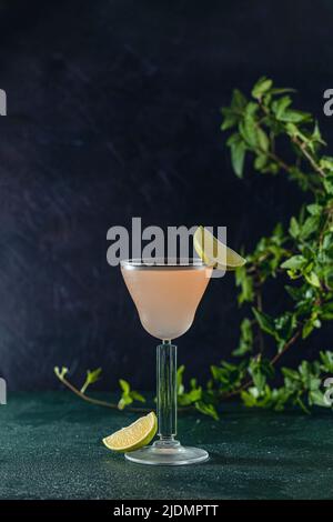 Glass of refreshing Pegu Club cocktail served on dark green table surface surround of fresh lime, shallow depth of the field. Stock Photo