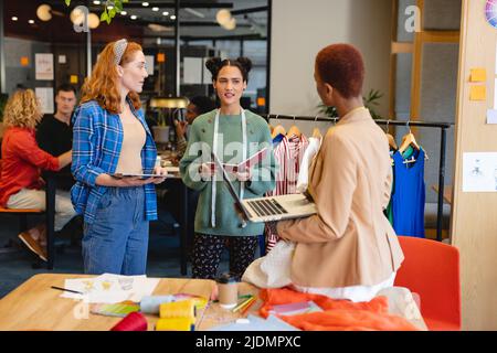 Multiracial female fashion designers discussing over laptop in office ...