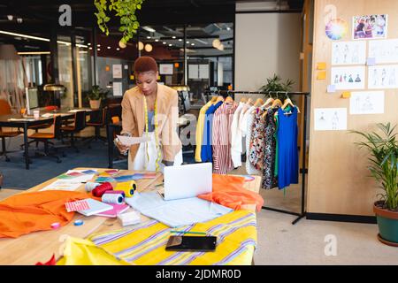 African american female fashion designer reading document at desk in studio Stock Photo