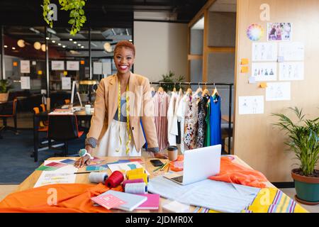 Portrait of smiling african american female fashion designer at desk in studio Stock Photo