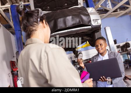 African american mid adult engineer using laptop while working with asian female colleague Stock Photo