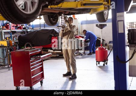 Mid adult female asian welder repairing car on lift in workshop, copy space Stock Photo