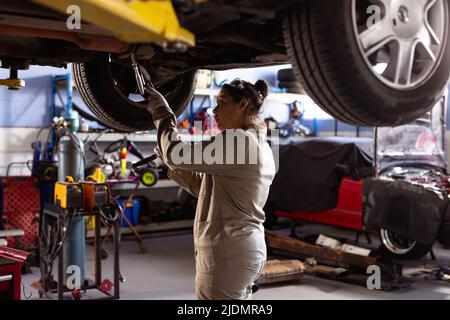 Side view of mid adult asian female technician using work tool while repairing car in workshop Stock Photo