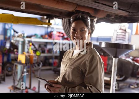 Portrait of smiling mid adult asian mechanic repairing car using digital tablet in workshop Stock Photo