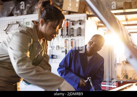 Mid adult female multiracial mechanics working together while repairing car in workshop Stock Photo