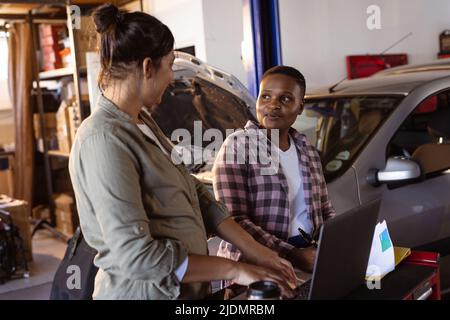 Confident mid adult multiracial female welders using laptop while working together in workshop Stock Photo