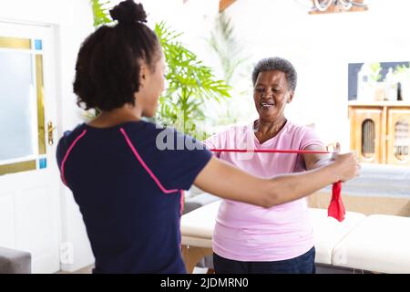 African american female physiotherapist helping senior woman in exercising with resistance band Stock Photo