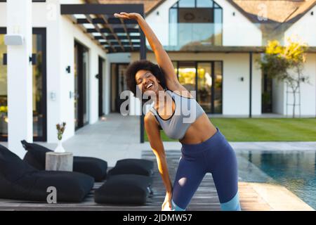 Cheerful young african american woman doing stretching exercise in backyard Stock Photo