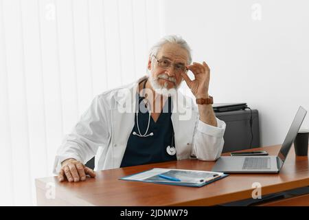 Senior healthcare worker doing some paperwork and using laptop while working at doctor's office Stock Photo