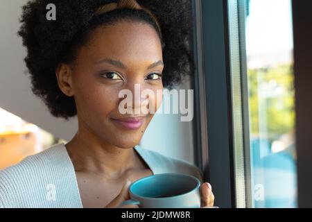 Portrait of confident smiling young african american afro woman holding coffee cup at home Stock Photo