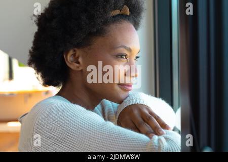 Side view of thoughtful young african american afro woman looking through window at home Stock Photo