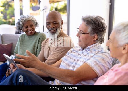 Caucasian senior man using digital pc while sitting with multiracial friends on sofa in nursing home Stock Photo