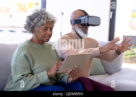 African american senior woman using digital pc and man using virtual reality simulator on sofa Stock Photo