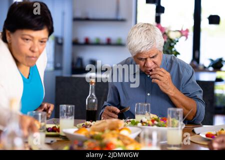 Biracial senior man and woman eating food while sitting at dining table in nursing home Stock Photo