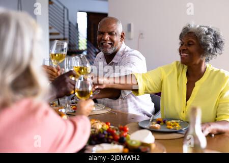 Multiracial cheerful senior friends toasting wineglasses while having lunch at dining table Stock Photo