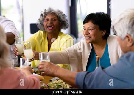 Multiracial cheerful senior friends toasting drinks while having lunch at dining table Stock Photo