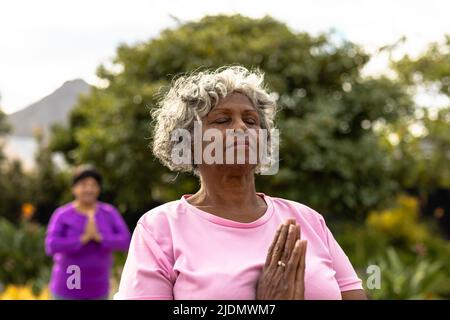 African american senior woman with eyes closed meditating against trees in yard at nursing home Stock Photo
