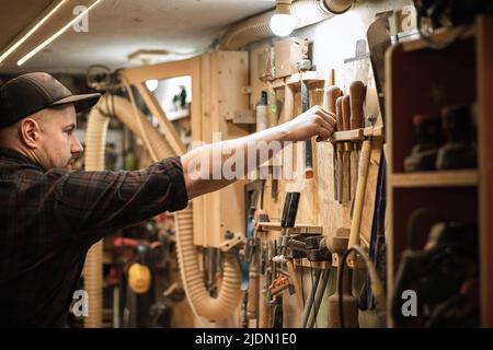 Side view of carpenter, professional businessman holding and putting joinery equipment tools in special frame shelf wall Stock Photo