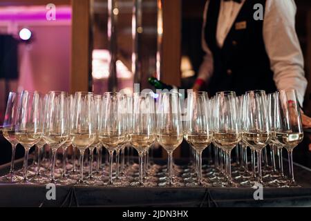 Waiter serving row of glasses of white champagne on tray in restaurant closeup. Pouring sparkling wine into glasses, event celebration. Banquet hall Stock Photo
