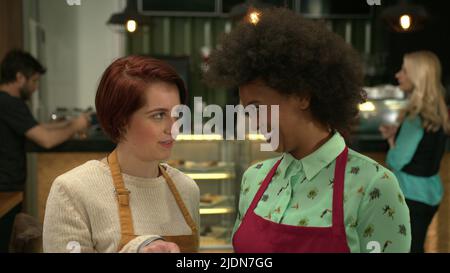 Female manager explaining small business Coffee shop to new employee. Two diverse employees wearing aprons standing inside cafe Stock Photo