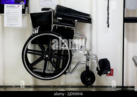 wheelchair hanging on a wall in a crew area for emergency case and a fire extinguisher next to it with phone Stock Photo