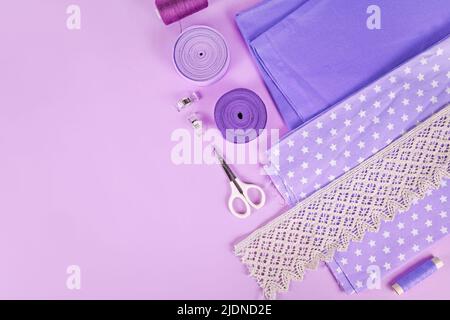 Sewing flat lay with various tools like fabric, scissors, spools and ribbons on violet background Stock Photo