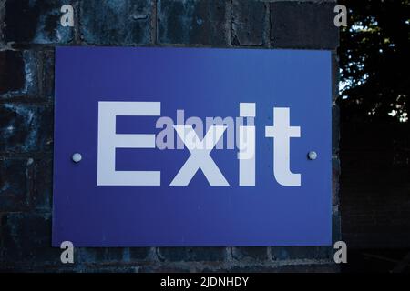 Exit sign in white lettering on blue background fixed to a brick wall Stock Photo