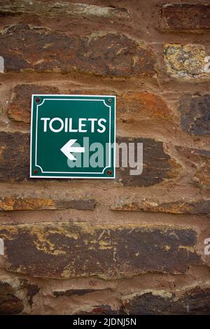 Toilets sign and arrow in white letters on a green background fixed to an old stone wall Stock Photo