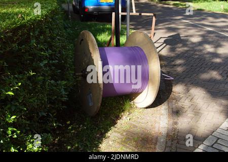 Wooden reel with thin purple, fiber optic cable on the side of the street of the Dutch village of Bergen. June, Stock Photo