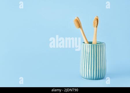 Two bamboo toothbrushes in a ceramic holder on a blue background. Eco-friendly, zero-waste concept. Copy space for text, selective focus Stock Photo
