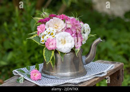 bouquet of roses, hydrangea flowers and sneezeweed in vintage tea pot in garden Stock Photo