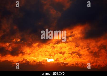Sunset on dramatic sky, orange sun shining through dark clouds. Picturesque cloudscape for horror background Stock Photo