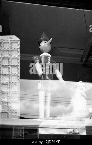 A wooden Pinocchio toy standing in a storefront window. Image captured on analog black and white film. Exeter, New Hampshire USA. Stock Photo