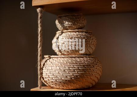 Basket for small things. Object in interior. Braided box is rounded in shape. Sunlight on object in room. Three boxes stand on top of each other. Stock Photo