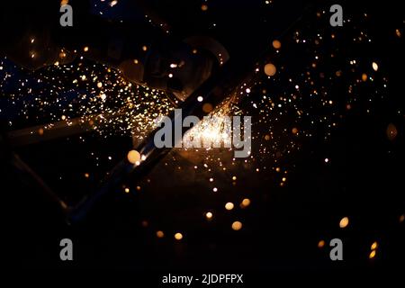 Sparks from grinding metal. Steel processing in workshop. Lights in dark. Production of parts. Cutting became grinder. Processing of welding seams. Stock Photo