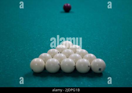 Billiard balls are collected in triangle. White balls on pool table. Details of sports equipment. Green cloth on table. Preparation of game. Stock Photo