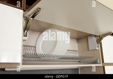 Dish dryer integrated in a wall cabinet with a door that opens upwards. Stock Photo