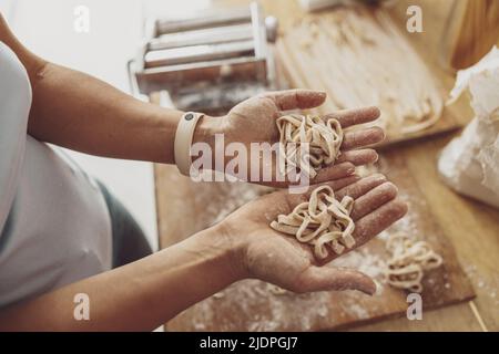A woman in her kitchen holds in her palms the homemade noodles she has just cooked. Stock Photo