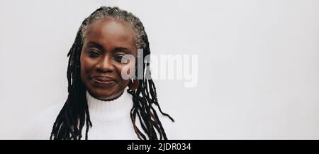 Confident woman with dreadlocks looking at the camera while standing against a white background. Mature black woman embracing her natural hair. Stock Photo