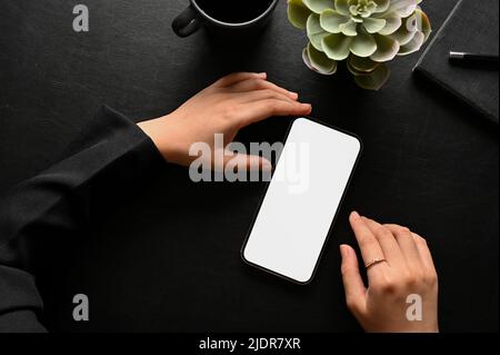 A female's hands using a mobile phone touchscreen at her stylish black workspace tabletop. overhead view and close-up image of a cellphone white scree Stock Photo