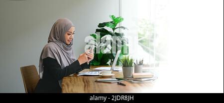 Muslim asian woman using mobile phone and laptop computer at modern office. Stock Photo