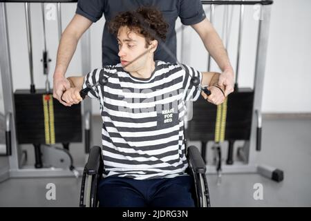 Rehabilitation specialist helps a guy in a wheelchair to do exercise Stock Photo