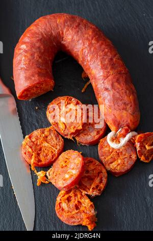 Spanish chorizo sliced on a slate chopping board with a knife. Stock Photo