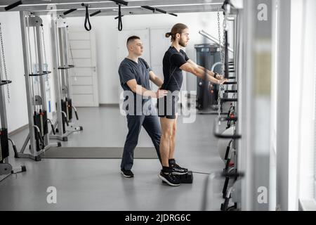 Man doing exercises on decompression simulators with the help of rehabilitation specialist Stock Photo