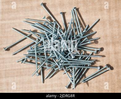Pile of shiny new self-tapping screws lay on a cardboard sheet, close-up background photo with selective soft focus Stock Photo