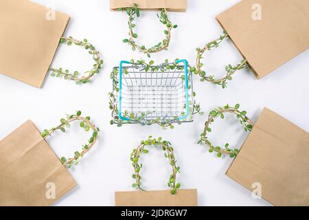 Kraft paper bag and Shopping supermarket basket whose handles are entwined entwined with plant. Responsible consumption. Eco-friendly business. Ecology and zero waste concept. flat lay Stock Photo